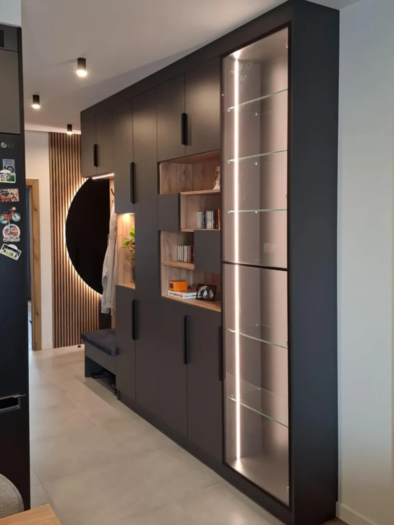 Zabudowa wejściowa z ciemną płytą meblową i dekoracyjnym półokrągłym podświetleniem LED – nowoczesny projekt mebli na wymiar w Olsztynie