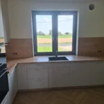 Biała kuchnia na wymiar w kształcie L z drewnianym blatem przy oknie